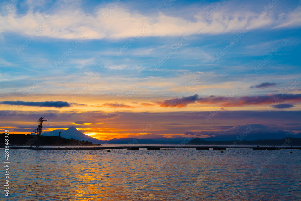 Wide shot of beautiful sunrise colors on the shore of Lake Llanquihue with iconic volcanoes in the background