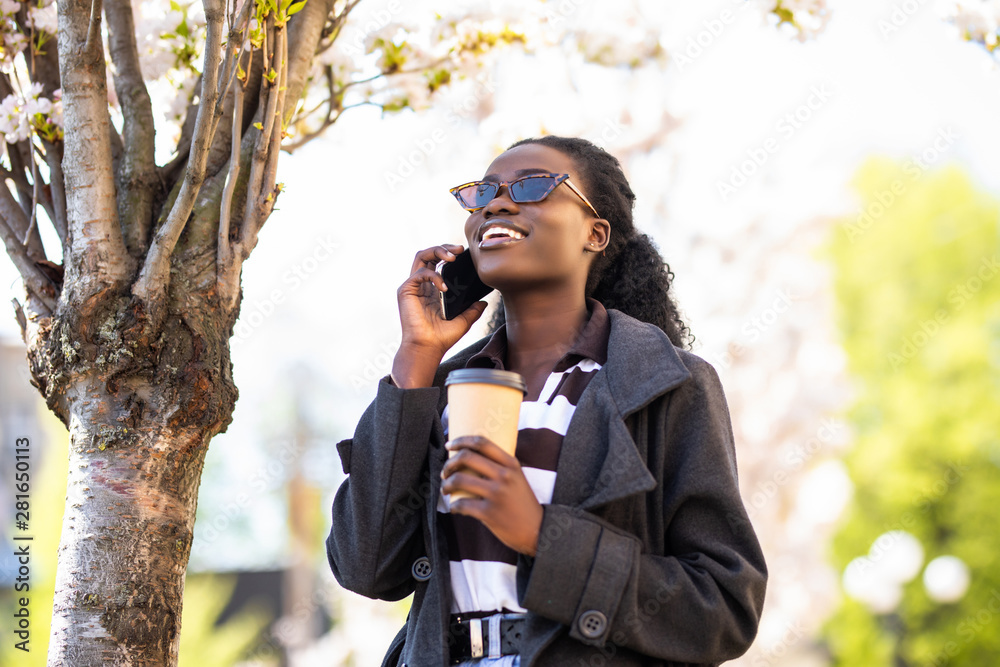 African young woman talking on the phone with a coffee on the sunny street African young woman talking on the phone with a coffee on the sunny street