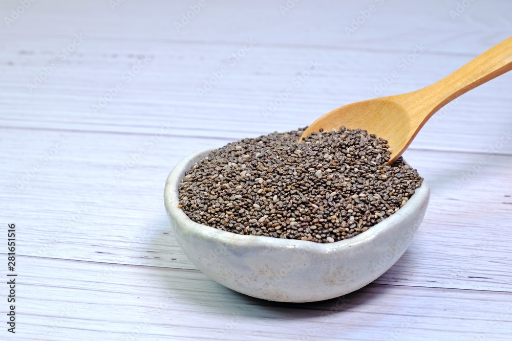 Little wooden spoon picking Chia seeds from small white ceramic bowl. Little wooden spoon picking Chia seeds from small white ceramic bowl.