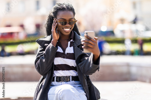 Cheerful african tudent girl talking at video call with smartphone in the street