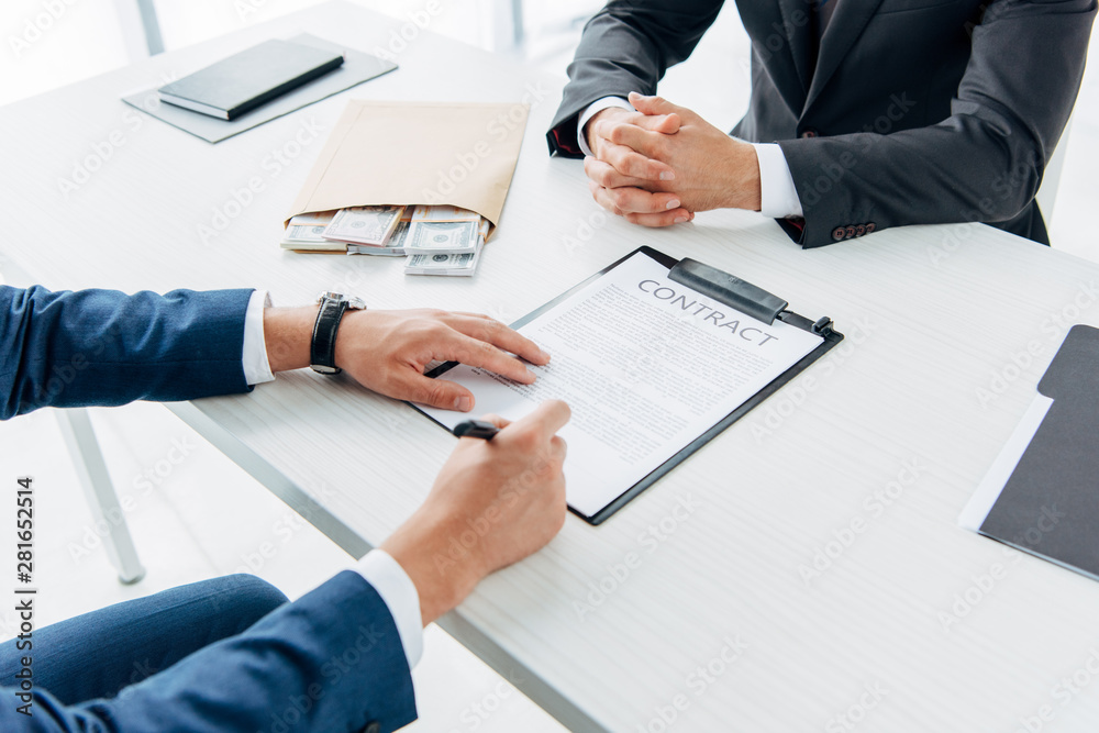 selective focus of man holding clipboard and pointing with finger at contract with pen near business partner gesturing in office selective focus of man holding clipboard and pointing with finger at contract with pen near business partner gesturing in office