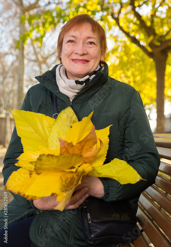 Happy elderly woman with a bouquet of maple leaves in autumn park photo