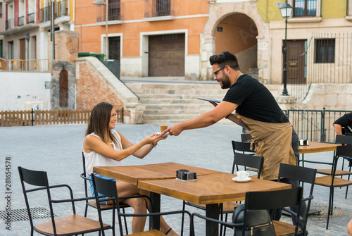 A waiter is serving a coffee to a young woman on a pub terrace