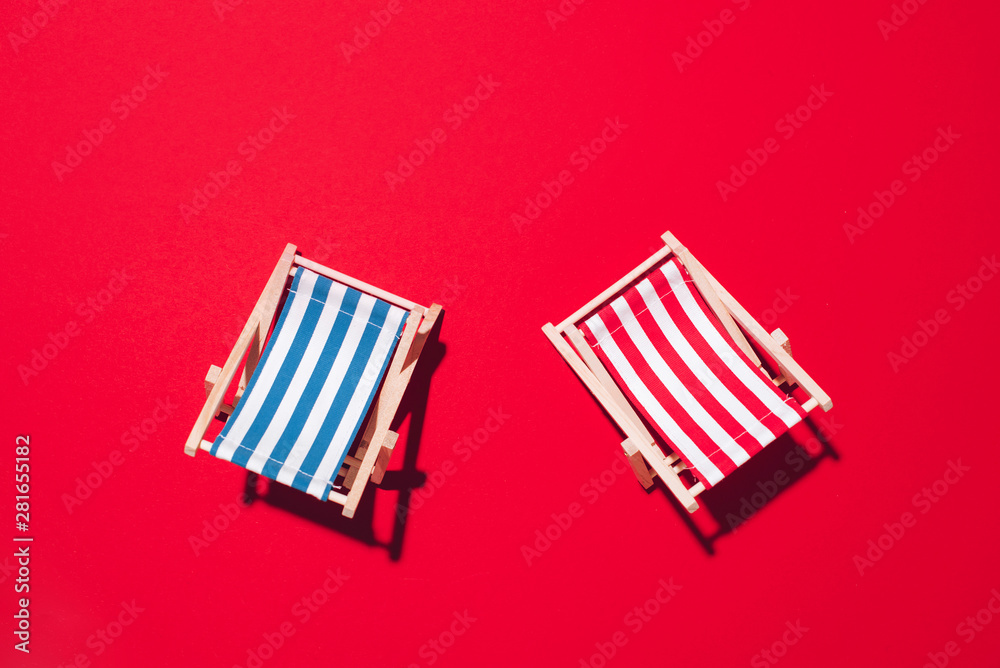 Two deck chairs with hard shadow on red paper background. Flat lay and copy space. Summer travel vacation concept. Minimal composition Two deck chairs with hard shadow on red paper background. Flat lay and copy space. Summer travel vacation concept. Minimal composition