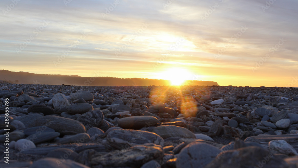 Sunset on a rock beach with lens flare and cliffs with dramatic clouds Sunset on a rock beach with lens flare and cliffs with dramatic clouds