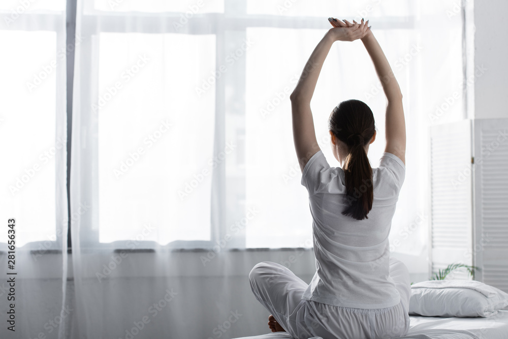 back view of woman with ponytail sitting on bed and stretching in clinic back view of woman with ponytail sitting on bed and stretching in clinic