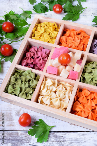Multicolored pasta farfalle and cubes of cheese in wooden box