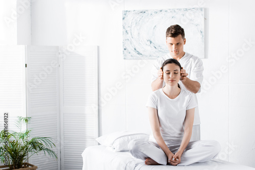 young woman sitting with closed eyes while masseur touching her ears