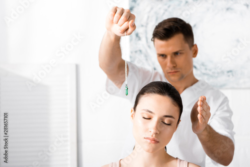 focused hypnotist standing near woman with closed eyes and holding green stone