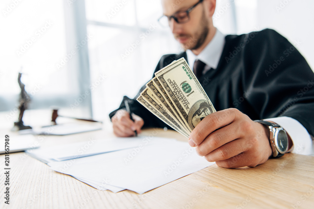 selective focus of judge holding dollar banknotes and writing in office selective focus of judge holding dollar banknotes and writing in office