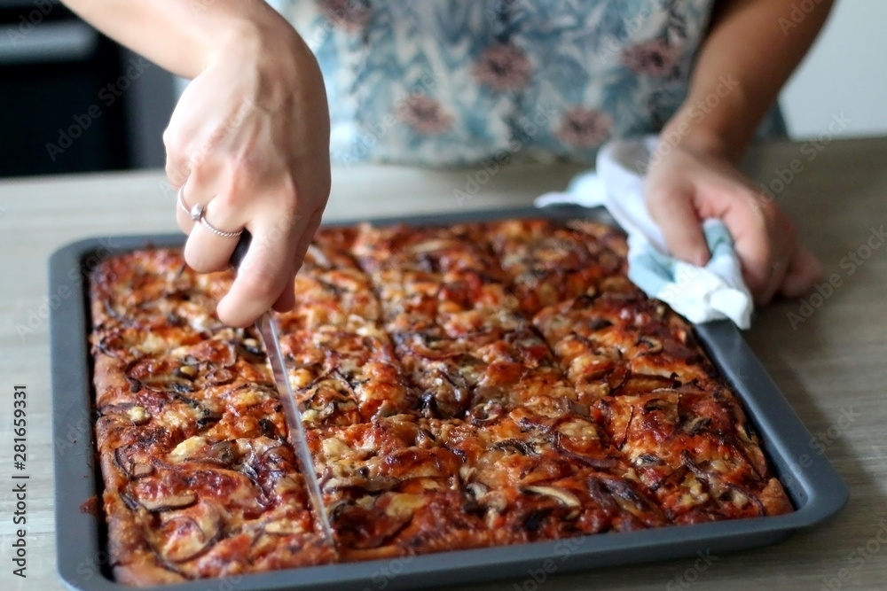 Unrecognizable person cutting homemade vegetarian pizza with tomato sauce, cheese, mushrooms and onion. Selective focus.