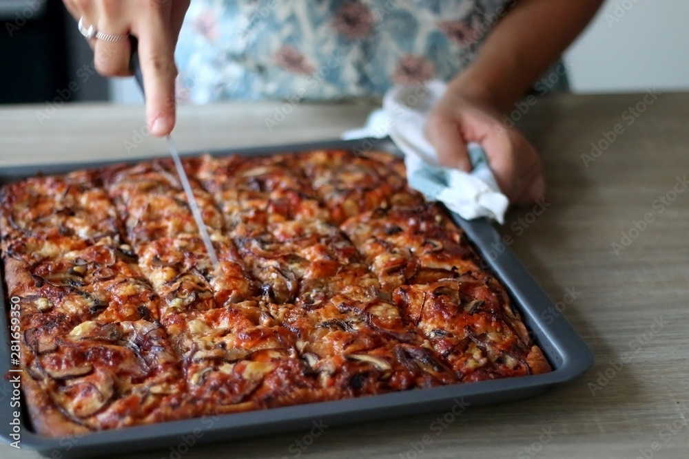 Unrecognizable person cutting homemade vegetarian pizza with tomato sauce, cheese, mushrooms and onion. Selective focus.