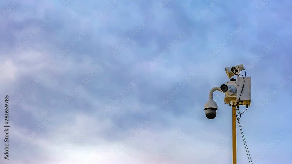 Panorama frame Outdoor security camera isolated against a cloudy blue sky background