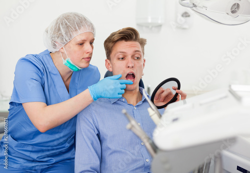 Patient showing dentist the problem in the mirror at the dental clinic