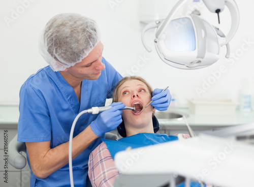 Male dentist treating young female patient in dental office