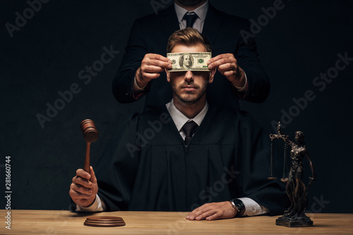 cropped view of man standing and covering face of judge with bribe on black