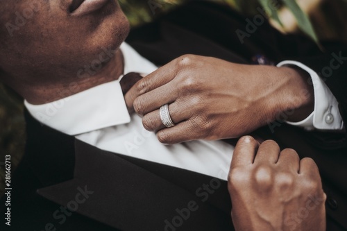 Closeup of an African-American male wearing a ring and a black suit jacket fixing his necktie photo