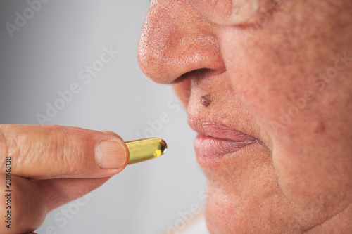 Vitamin And Supplement. Closeup Of Beautiful Old Woman Taking Yellow Fish Oil Pill. Female Hand Putting Omega-3 Capsule In Mouth. Healthy Eating And Diet Nutrition Concepts. High Resolution Image