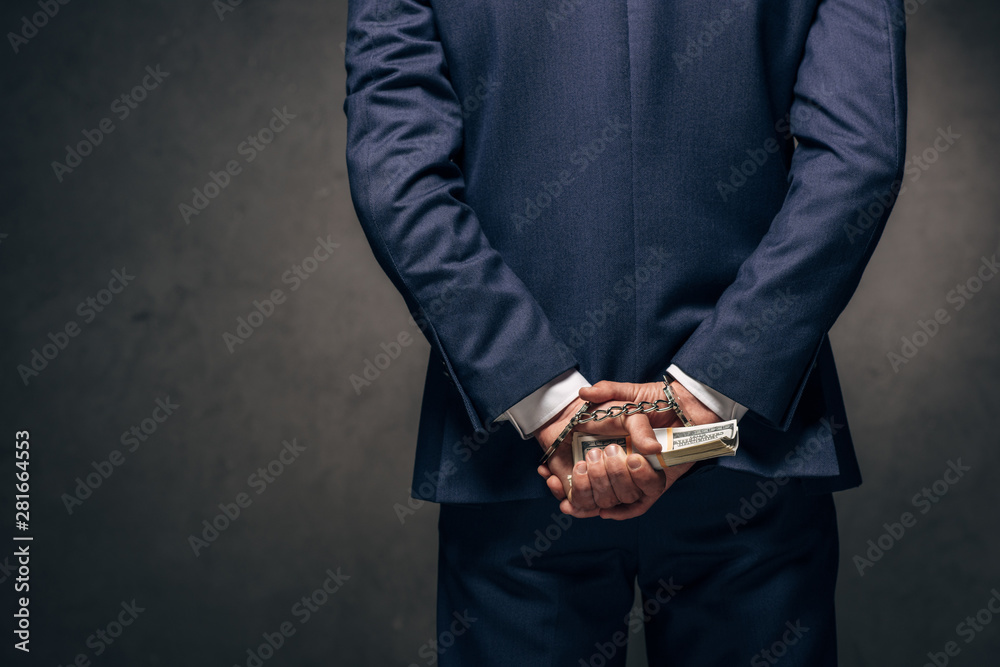 cropped view of handcuffed man in formal wear holding bribe on grey