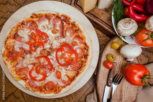 salami pizza on a wooden board, wooden background decorated with vegetables and cutlery
