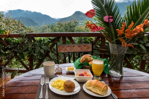 Having breakfast in the Ecuadorian Amazon. On the table you can see a plate with scrambled eggs, a cup of coffee, orange juice, bread, fruits, jam, butter and a beautiful vase with local flowers.