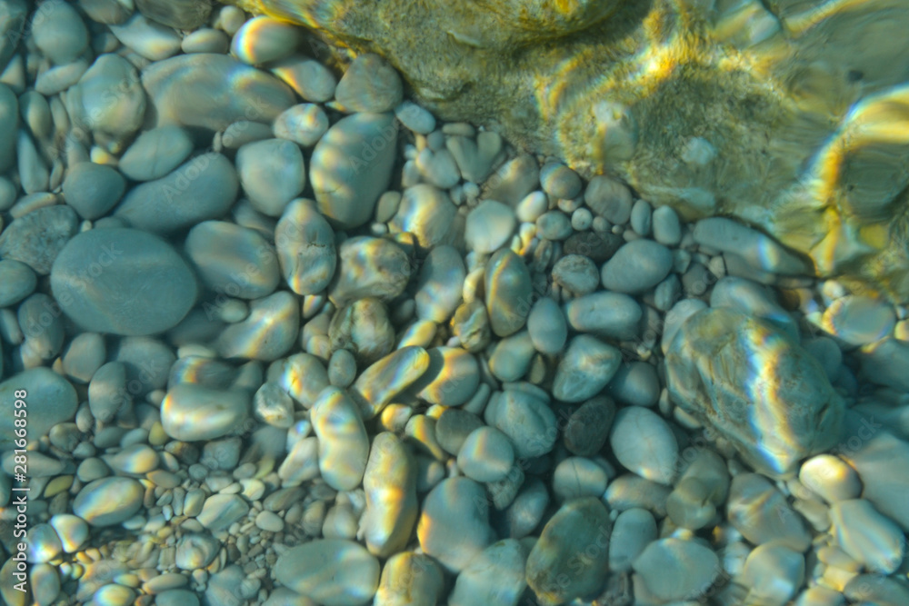 Fototapeta premium Beautiful colorful pebbles and big stone under turquoise blue clear water, scenic marine background or texture, top view