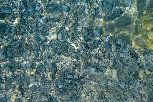 Beautiful colorful pebbles and big stone under turquoise blue clear water, scenic marine background or texture, top view