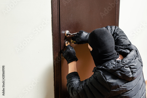 Thief in black mask trying to pick lock a door. House thief concept.