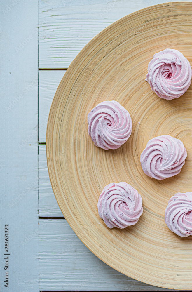 Merengue Marshmallow Zephyr lined in a circle on a bamboo plate on a white wooden background. Flat lay. Top view. Pink sweet homemade zephyr or marshmallow. Merengue Marshmallow Zephyr lined in a circle on a bamboo plate on a white wooden background. Flat lay. Top view. Pink sweet homemade zephyr or marshmallow.