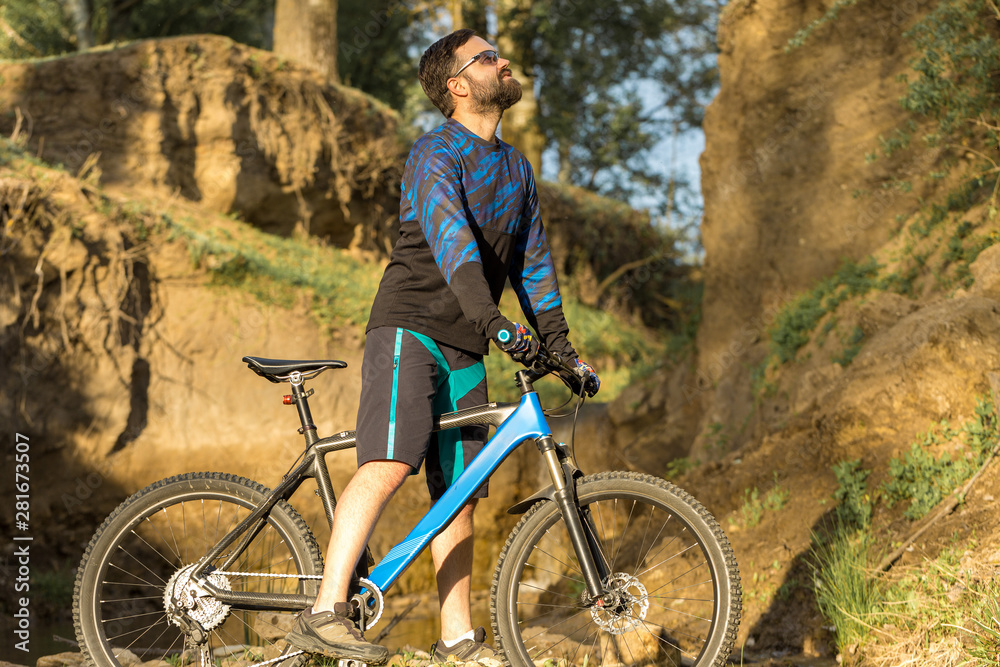 Fototapeta premium Cyclist in shorts and jersey on a modern carbon hardtail bike with an air suspension fork rides off-road on the orange-red hills at sunset evening in summer