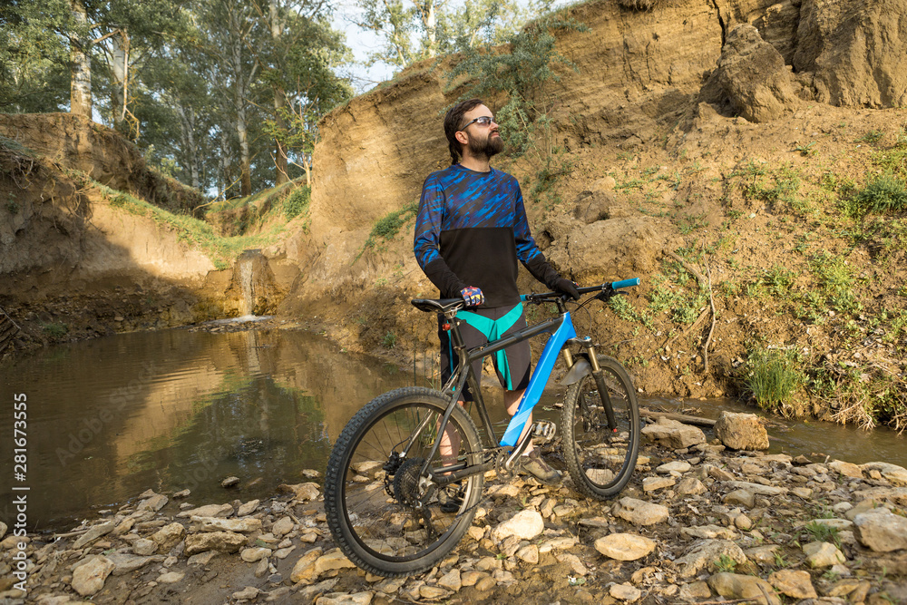 Cyclist in shorts and jersey on a modern carbon hardtail bike with an air suspension fork rides off-road on the orange-red hills at sunset evening in summer Cyclist in shorts and jersey on a modern carbon hardtail bike with an air suspension fork rides off-road on the orange-red hills at sunset evening in summer