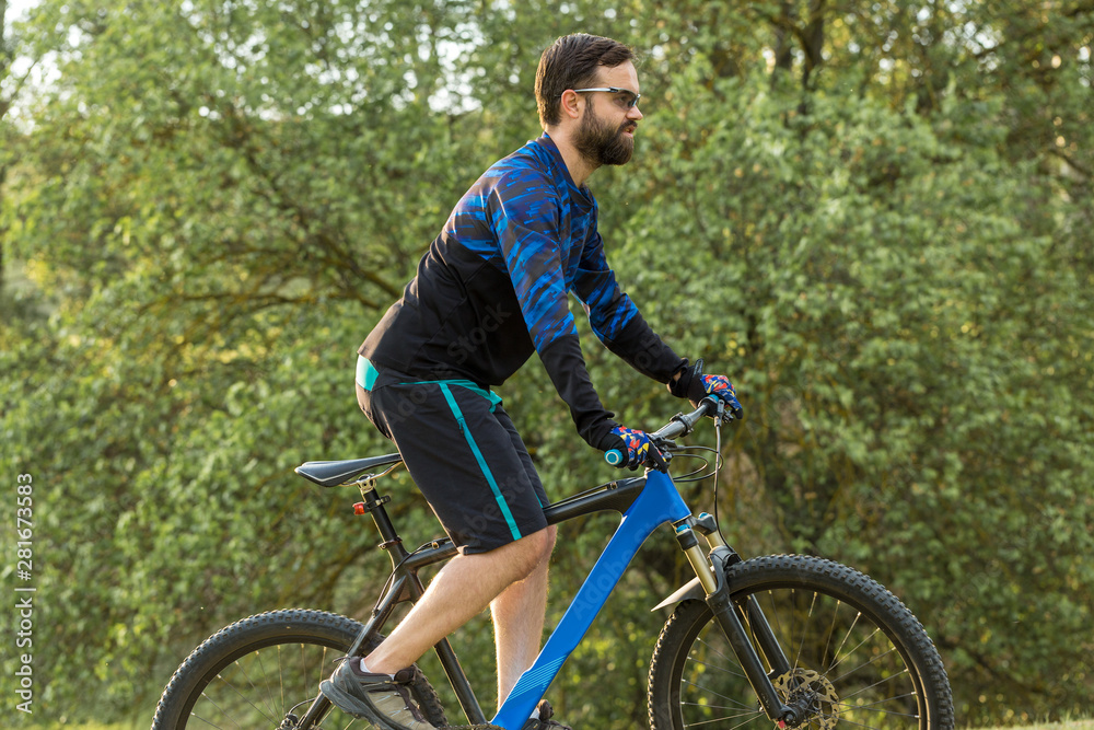 Cyclist in shorts and jersey on a modern carbon hardtail bike with an air suspension fork rides off-road on the orange-red hills at sunset evening in summer Cyclist in shorts and jersey on a modern carbon hardtail bike with an air suspension fork rides off-road on the orange-red hills at sunset evening in summer