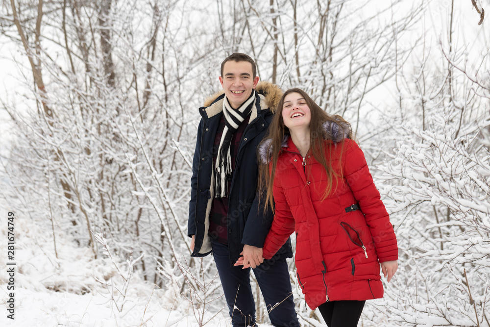 The guy and the girl have a rest in the winter woods. Husband and wife in the snow. Young couple walking in winter park The guy and the girl have a rest in the winter woods. Husband and wife in the snow. Young couple walking in winter park