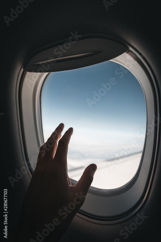 Porthole window in the plane with a man's hand during the flight.