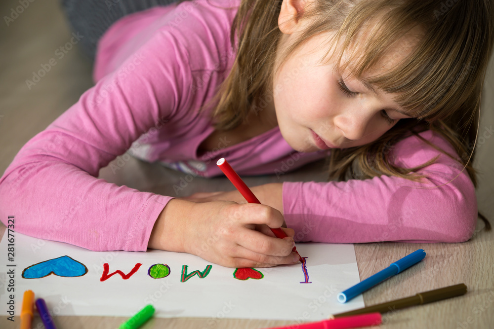 Cute child girl drawing with colorful crayons I love Mom on white paper. Art education, creativity concept. Cute child girl drawing with colorful crayons I love Mom on white paper. Art education, creativity concept.