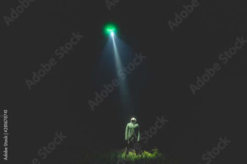 The UFO shines on a male standing on the grass. night time