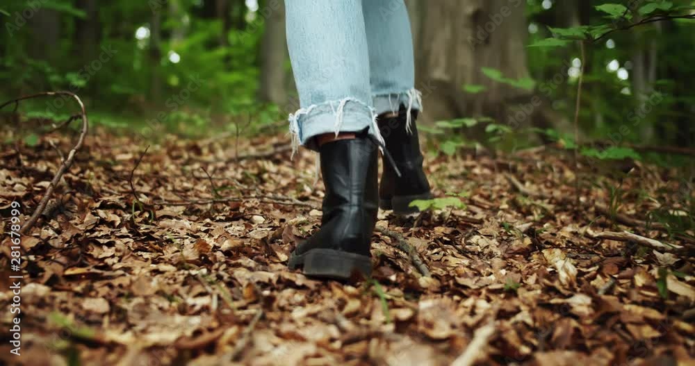 Female tourist in hiking boots and jeans walking in forest, backview Female tourist in hiking boots and jeans walking in forest, backview