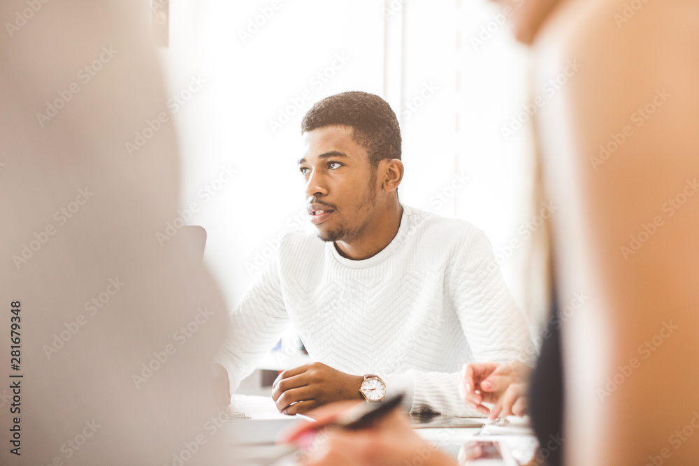 A team of young office workers, businessmen with laptop working at the table, communicating together in an office. Portrait of a successful black man
