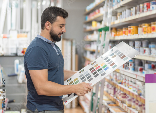 Obraz na plátně Man in drugstore selecting paint color for his work