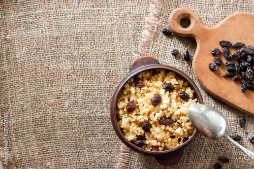 Sweet millet porridge with dark raisins in ceramic rustic bowl with rasins on wooden cutting board photo