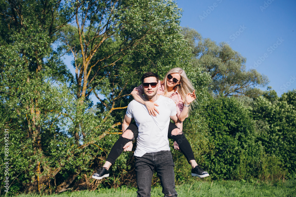 Girl sitting on the back of a man hugging and smiling in nature in summer