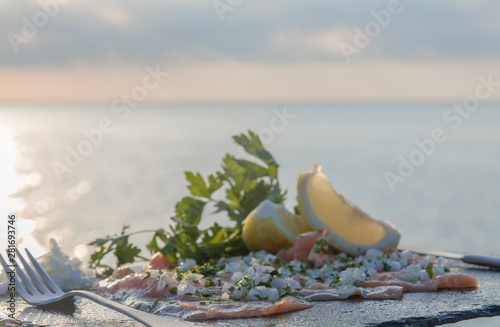 Close-up of a fillet of raw salmon, celery, white onion and lemon on a stone table