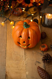 Halloween pumpkin with leaves on an old wooden table with luminous lights and an old lamp. Autumn mood, and atmospheric photo. Vertical photo, flat lay with space