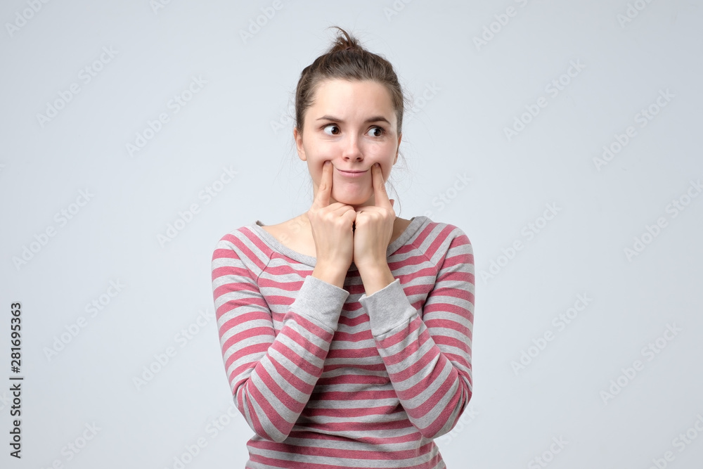 Young upset woman making fake smile with her fingers stretching the corners of her mouth. Try to stay positive after failing at something. Young upset woman making fake smile with her fingers stretching the corners of her mouth. Try to stay positive after failing at something.
