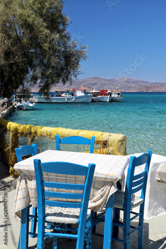 Typical blue chairs and table of Greece overlooking fishing harbour and turquoise Aegean Sea  Naxos  Greek Islands