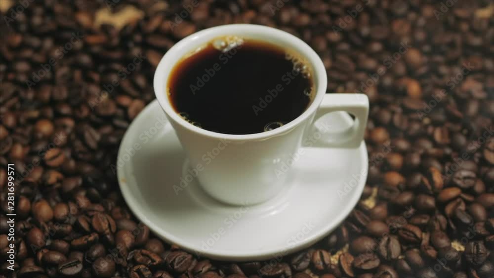 Coffee cup and coffee beans. White cup of evaporating coffee on the table with roasted bean. Stock footage. Coffee cup and coffee beans. White cup of evaporating coffee on the table with roasted bean. Stock footage.