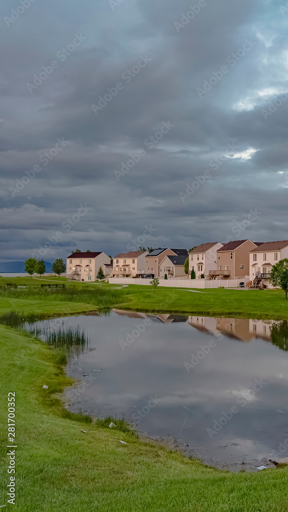 Vertical Scenic neighborhood park with a shiny pond and pathway under an overcast sky Vertical Scenic neighborhood park with a shiny pond and pathway under an overcast sky