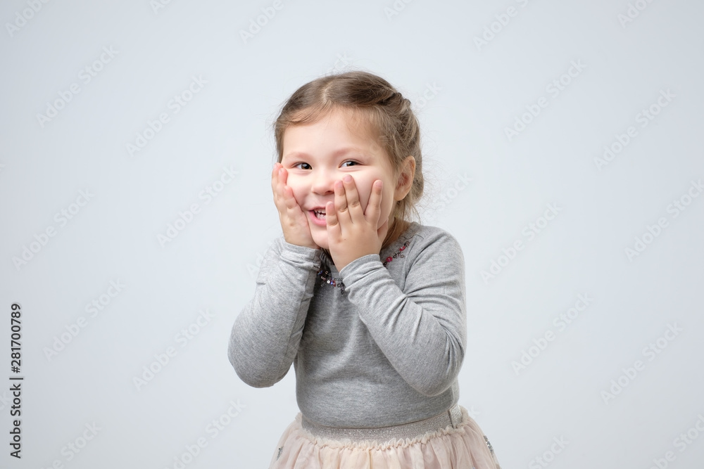 Small girl looking at camera, holding face with hands expressing excitement. Kid getting happy after receiving birthday present from mother. Studi shot Small girl looking at camera, holding face with hands expressing excitement. Kid getting happy after receiving birthday present from mother. Studi shot