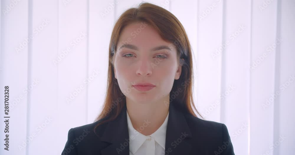 Closeup portrait of young successful businesswoman looking at camera confidently indoors in the white office Closeup portrait of young successful businesswoman looking at camera confidently indoors in the white office