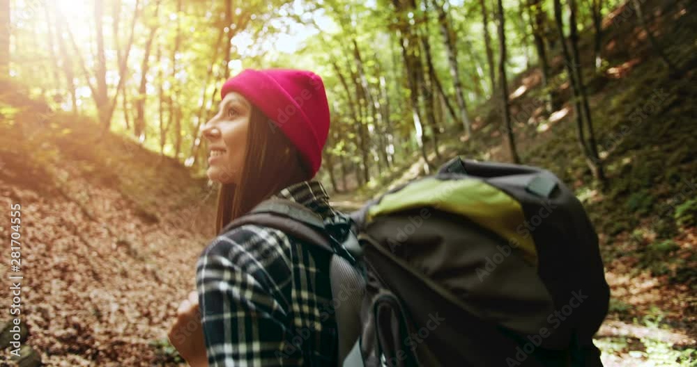 Smiling lady tourist in red hat with backpack walking in forest and looking around, freedom